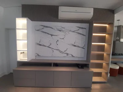 Painel de TV com revestimento de mármore e nichos iluminados em LED, marcenaria executada em Campinas